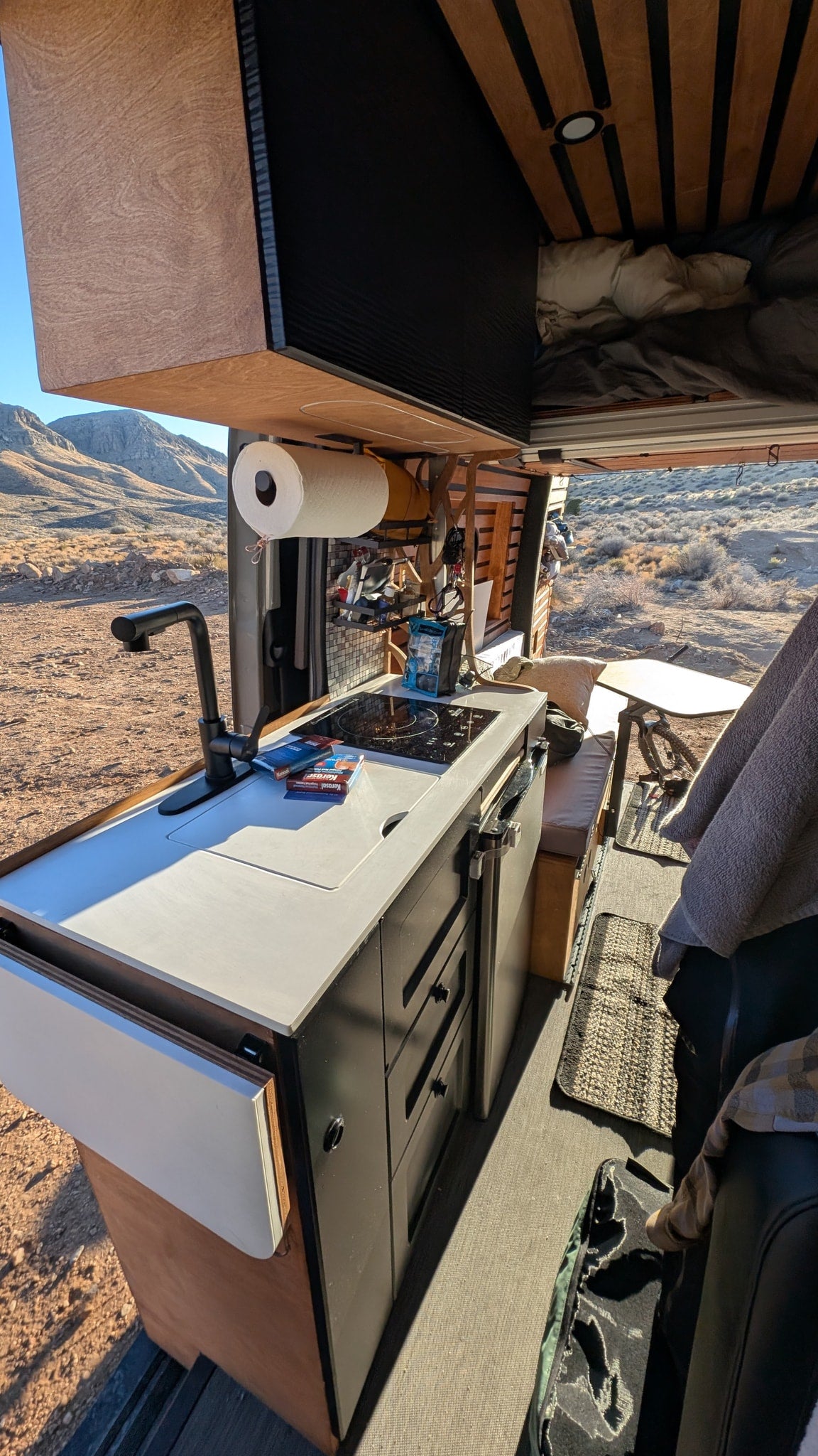 Cozy RV rental interior featuring a functional kitchen, overhead bed, and expansive desert views from the open side. — photo 8