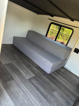 Experience comfort in this RV rental with a gray sofa bed, stylish wood-look floor, and bright window.