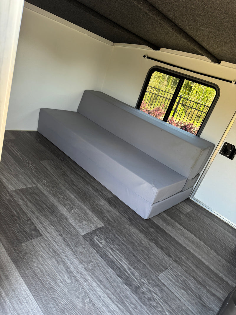 Experience comfort in this RV rental with a gray sofa bed, stylish wood-look floor, and bright window. — photo 7
