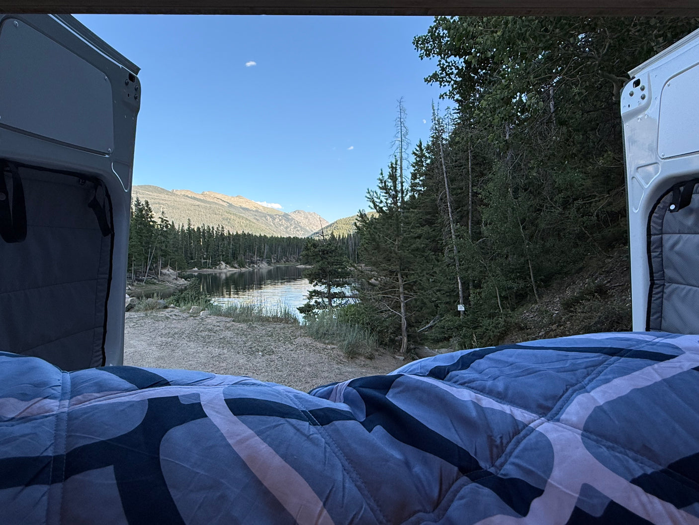 Cozy RV rental bed with serene lake & mountain view. Perfect for peaceful van life camping adventures.