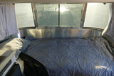 Inside an rv rental bedroom: a large bed with gray bedding, wide windows, and bright sunlight.
