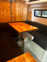 RV rental: Cozy dinette features a wooden table, black bench seating, and wood paneling in a modern van interior.