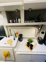 Modern RV rental kitchen featuring open upper cabinets, a sink, coffee maker, and convenient breakfast essentials.