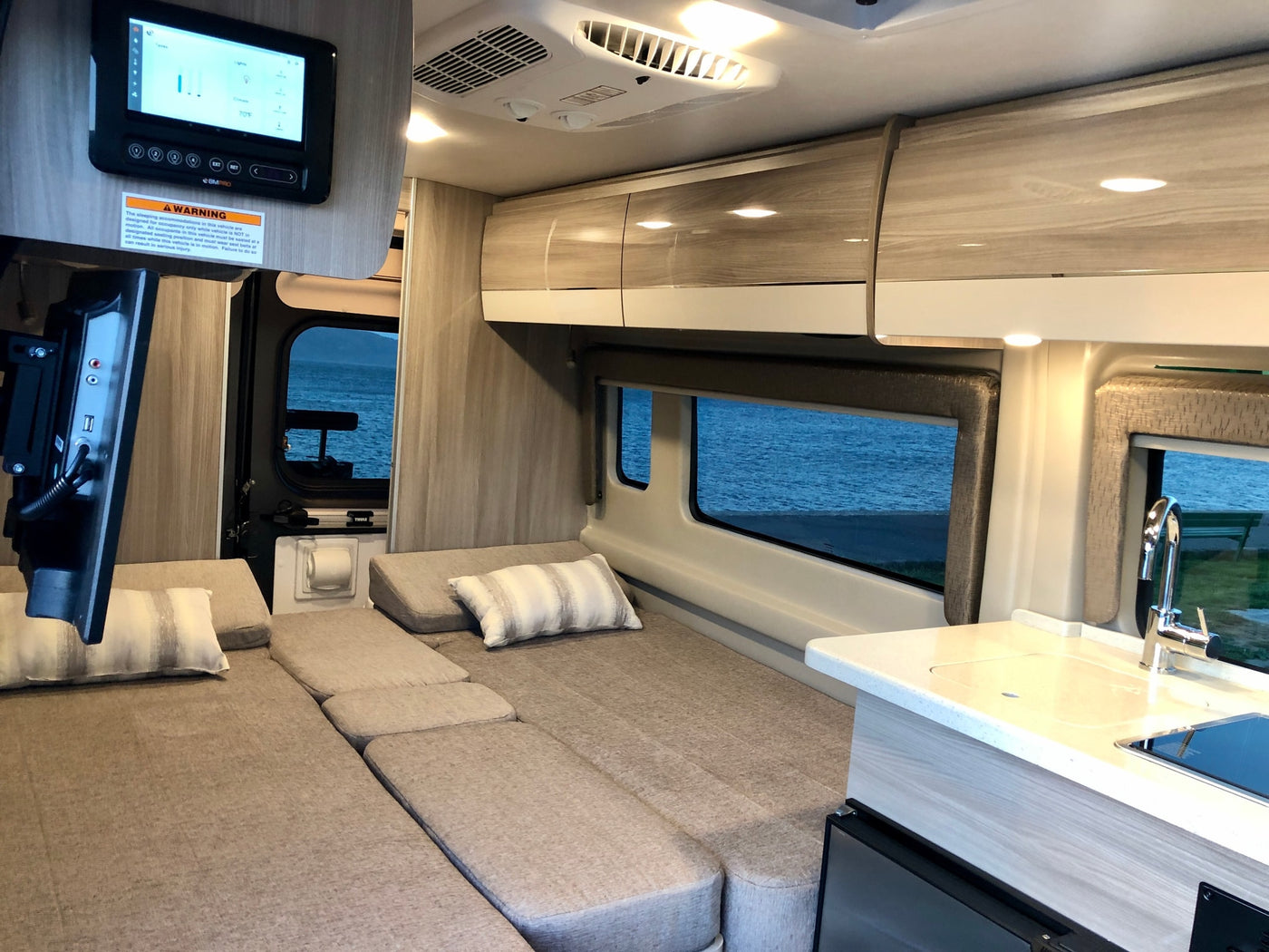 Spacious RV rental interior with multi-purpose seating/bed, compact kitchen, and digital control panel overlooking water. — photo 9