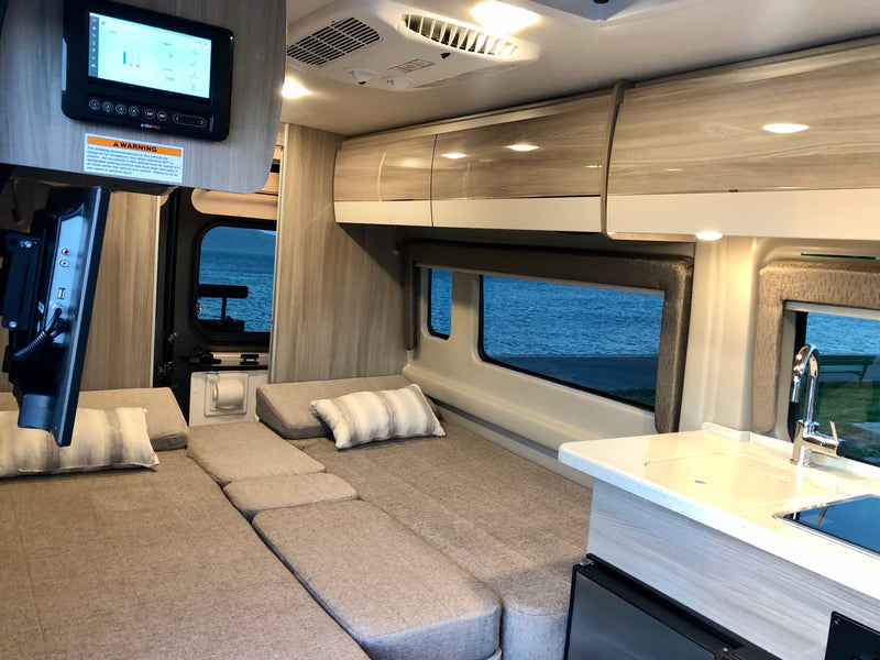 Spacious RV rental interior with multi-purpose seating/bed, compact kitchen, and digital control panel overlooking water. — photo 9