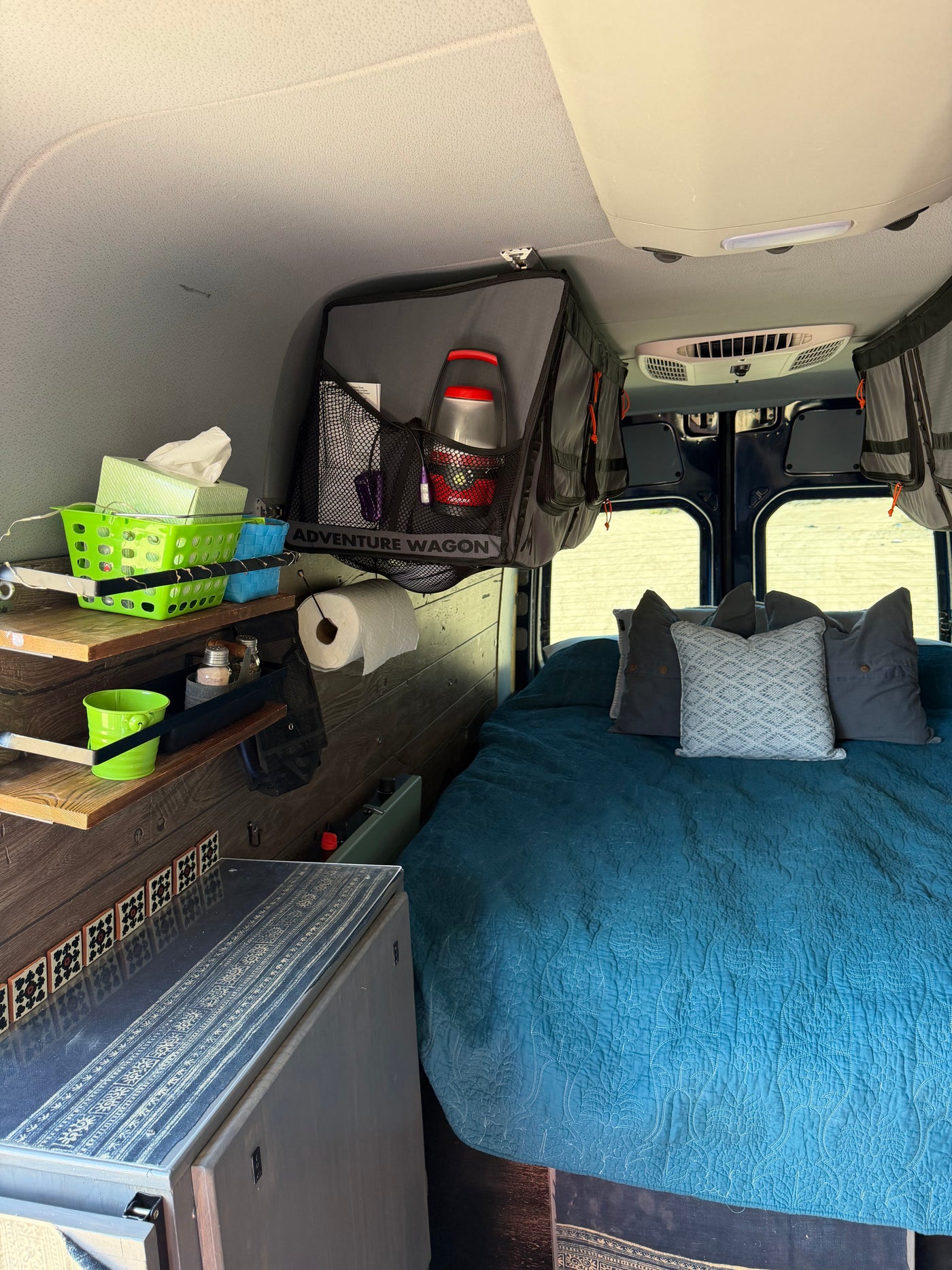 Comfortable RV rental sleeping area with a blue quilted bed, functional shelves, and overhead storage. — photo 13