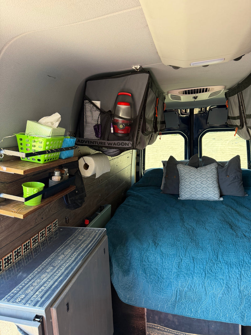 Comfortable RV rental sleeping area with a blue quilted bed, functional shelves, and overhead storage. — photo 13