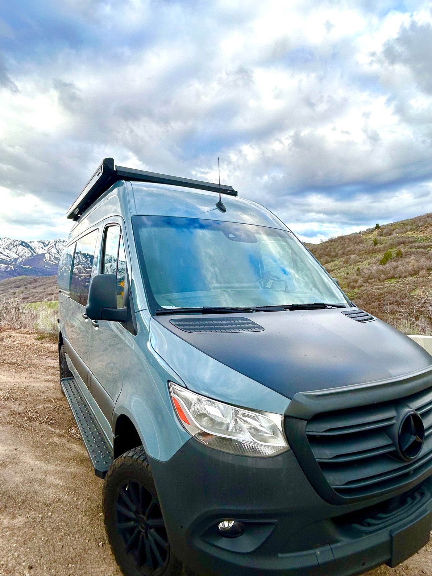 This customized Mercedes Sprinter van, perfect for an RV rental, is parked on a dirt road amidst scenic mountains under a cloudy sky. — photo 7