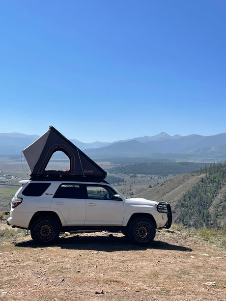 Experience mountain camping! White 4Runner with a rooftop tent deployed, ideal for an RV rental journey overlooking a valley.