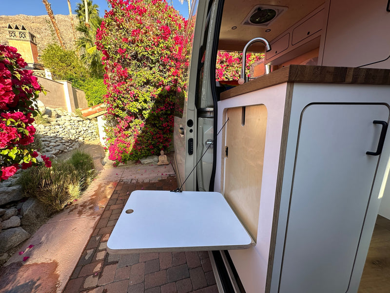 RV rental: Camper van with open door revealing kitchen & pull-out table, perfect for outdoor living in a lush garden. — photo 4