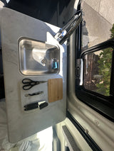 rv rental: functional kitchen counter featuring a stainless steel sink, faucet, cutting board, and kitchen tools by a window.