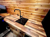 Modern RV rental kitchen area features wood countertops, integrated induction cooktop, and sleek black faucet.