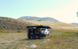 RV rental: Truck and teardrop trailer with awning & chairs set up at a scenic mountain campsite.