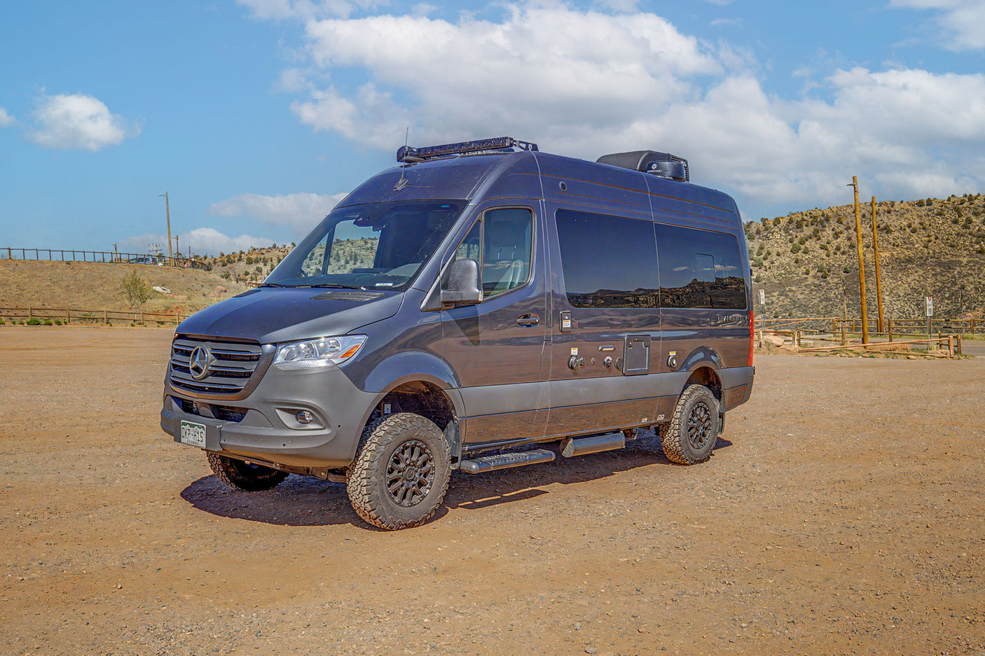 Adventure-ready dark grey Mercedes Sprinter camper van on a dirt lot. Perfect for an off-road RV rental experience.