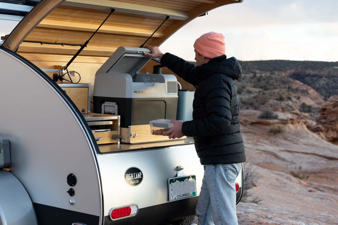  rear hatch open to reveal a Dometic fridge and organized camping gear.|Person uses a compact outdoor kitchen from an RV rental — photo 2
