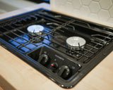 A Dometic two-burner gas cooktop in an RV rental, with one burner lit showing a blue flame, ideal for camp cooking.