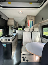 RV rental campervan interior featuring a compact kitchen, swiveling captain's chairs, and a round dining table.
