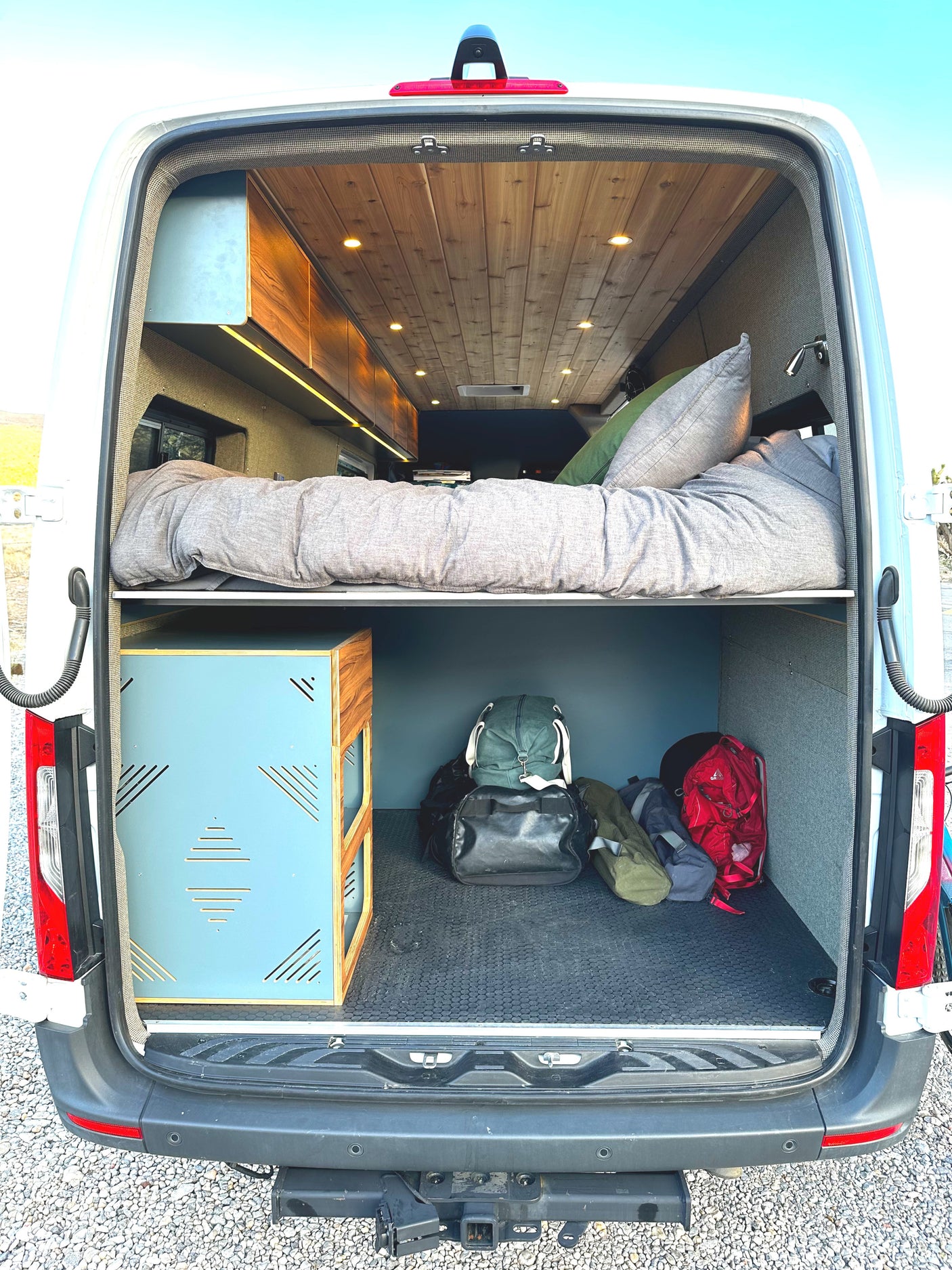 Experience an RV rental! This camper van's rear reveals a raised bed, cozy lighting, and spacious under-bed storage for your gear.