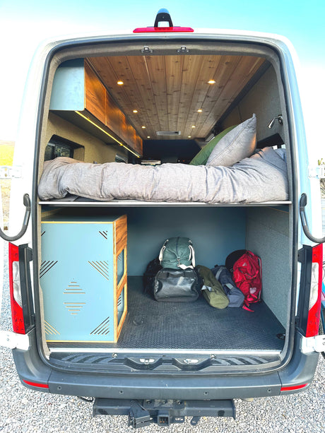 Experience an RV rental! This camper van's rear reveals a raised bed, cozy lighting, and spacious under-bed storage for your gear.