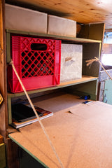Organized RV rental interior: Built-in shelves with a red crate, patterned bin, and desk space for compact camper living.