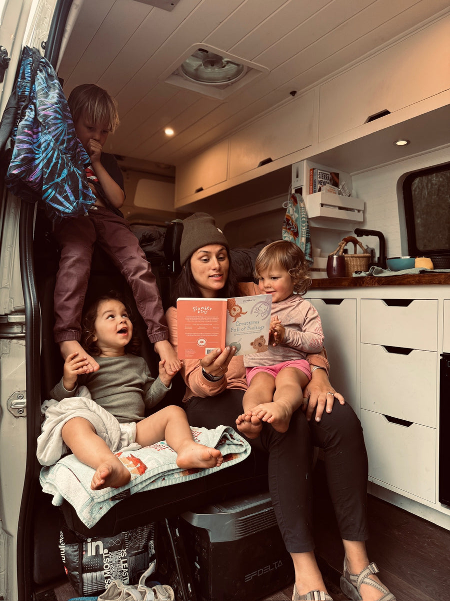 Cozy rv rental family time! Mom reads "Creatures Full of Feelings" to kids in their camper van, a perfect travel moment.