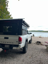 White Toyota Tacoma with a pop-top truck camper, an excellent rv rental for lakeside camping in Maine with a fire pit.