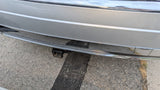 Silver RV rental rear bumper with chrome trim, minor scratches, and a trailer hitch, parked on asphalt.
