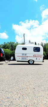 Compact white Scamp travel trailer, ideal for your next RV rental adventure. Towed by an SUV on a gravel lot.