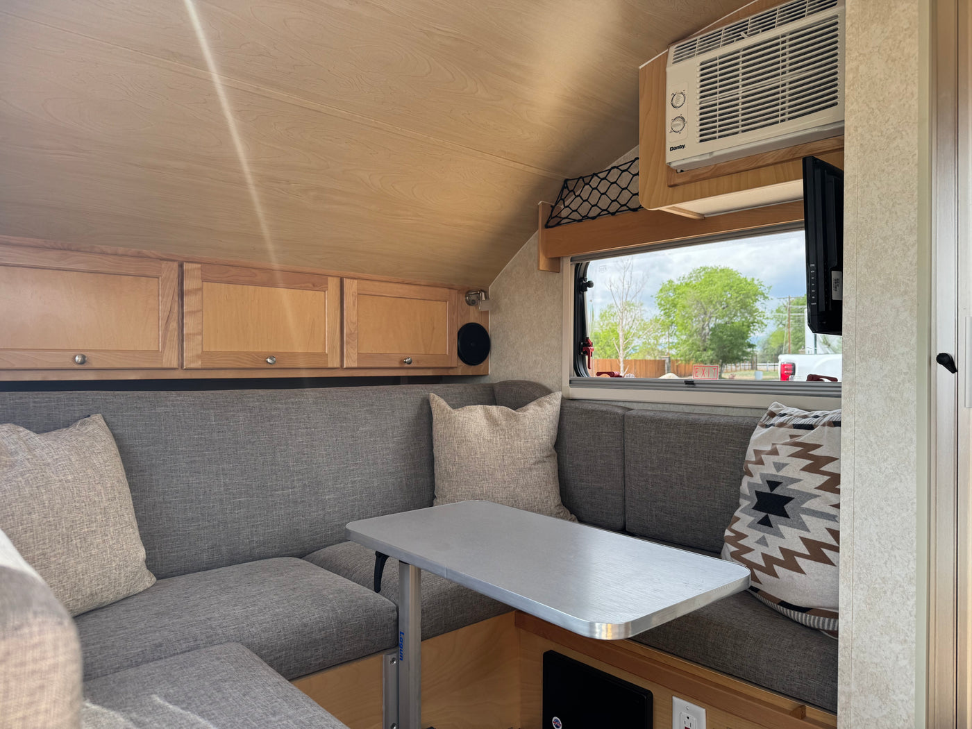 Comfortable RV rental interior featuring a U-shaped dinette, grey seating, wood cabinets, and an overhead AC unit. — photo 10