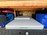 RV rental organized storage: Two white Lifetime tables, blue water jug, bags & pink mattress under wooden shelves in a van.