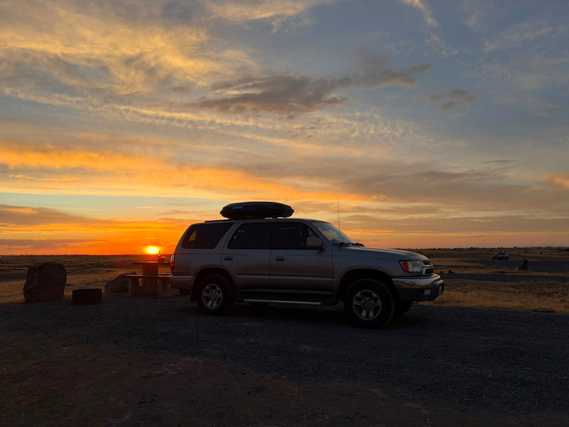 The 4Runner with its rooftop cargo box silhouetted against a wide sunset at a high-desert campsite — photo 11