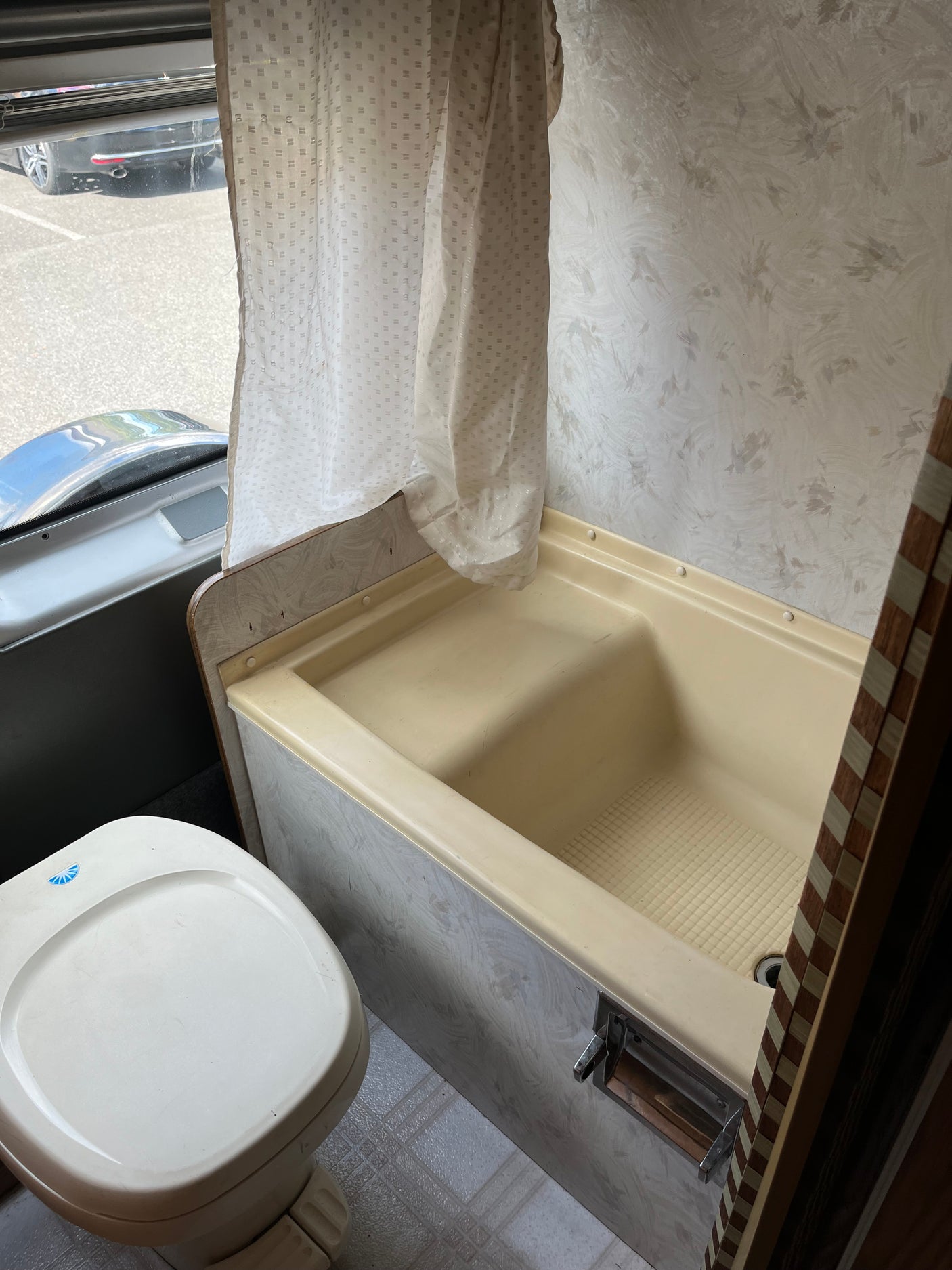 Compact RV rental bathroom, featuring a toilet, a small bathtub/shower with curtain, and window view to outside.