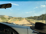 Enjoying the dusty road view from an RV rental, dashboard and hat in foreground, vast desert landscape beyond.