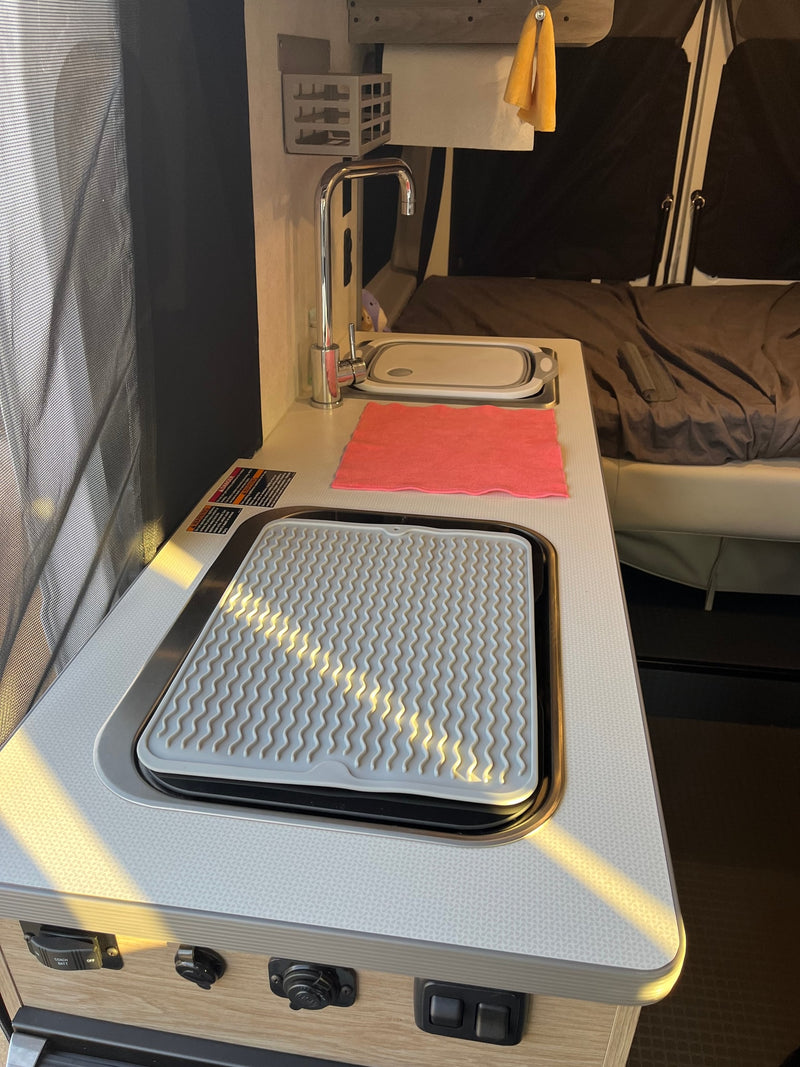 RV rental's compact kitchen: sink, faucet, drying mat on counter, with a bed in the background. — photo 9