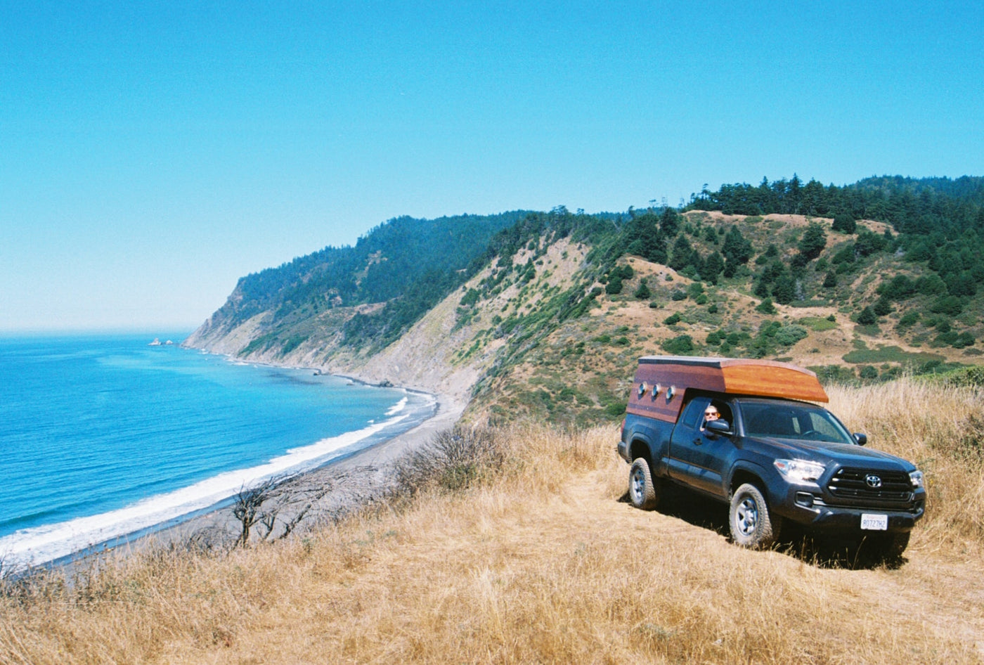  perfect RV rental for scenic coastal adventures. Ocean & mountains background.|RV rental truck overlooking stunning Pacific coast.|Cozy wooden interior of an **rv rental** features porthole windows — photo 2