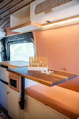 This inviting RV rental interior features a Connect Four game on a wooden table, warm peach walls, and custom wood cabinetry.