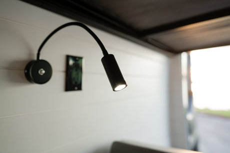 Illuminated black gooseneck LED light mounted on a white plank wall, characteristic of a modern RV rental interior.
