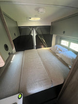 Cozy rv rental interior with a comfortable bed, overhead storage, and rear windows with privacy screens.