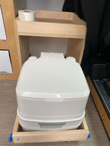 White portable Thetford toilet in custom wooden RV rental storage with toilet paper. Essential camper van amenity.