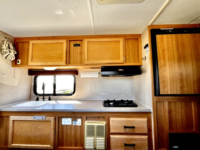  and a picnic table.|Enjoy scenic views from your RV rental kitchen! Black faucet overlooks green fields & snow-capped mountains under a blue sky.|RV rental: A grey truck with a white truck camper parked by a fence — photo 4