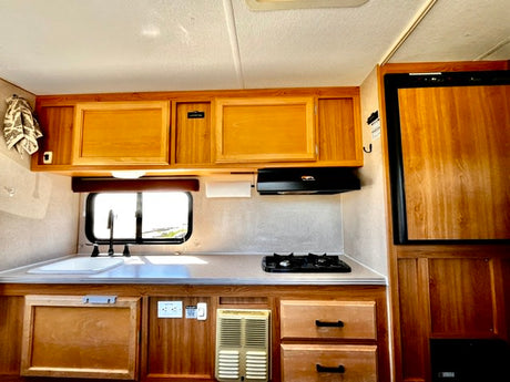 This RV rental kitchen features warm wood cabinets, a sink, two-burner stove, and a compact refrigerator for your travels.