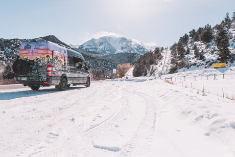 A colorful custom Aspen Custom Vans RV rental van parked on a snowy mountain road.