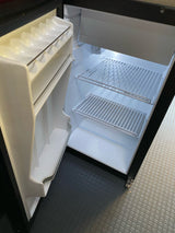 Clean, empty RV rental mini-fridge with door storage & wire shelves, illuminated by a bright interior light.
