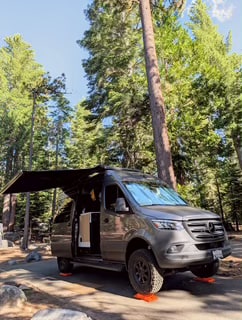  perfect for Lake Tahoe adventures. Parked by clear blue water under sunny pine trees.|Wake up to amazing views! This RV rental offers a cozy bed looking out to a serene beach — photo 3