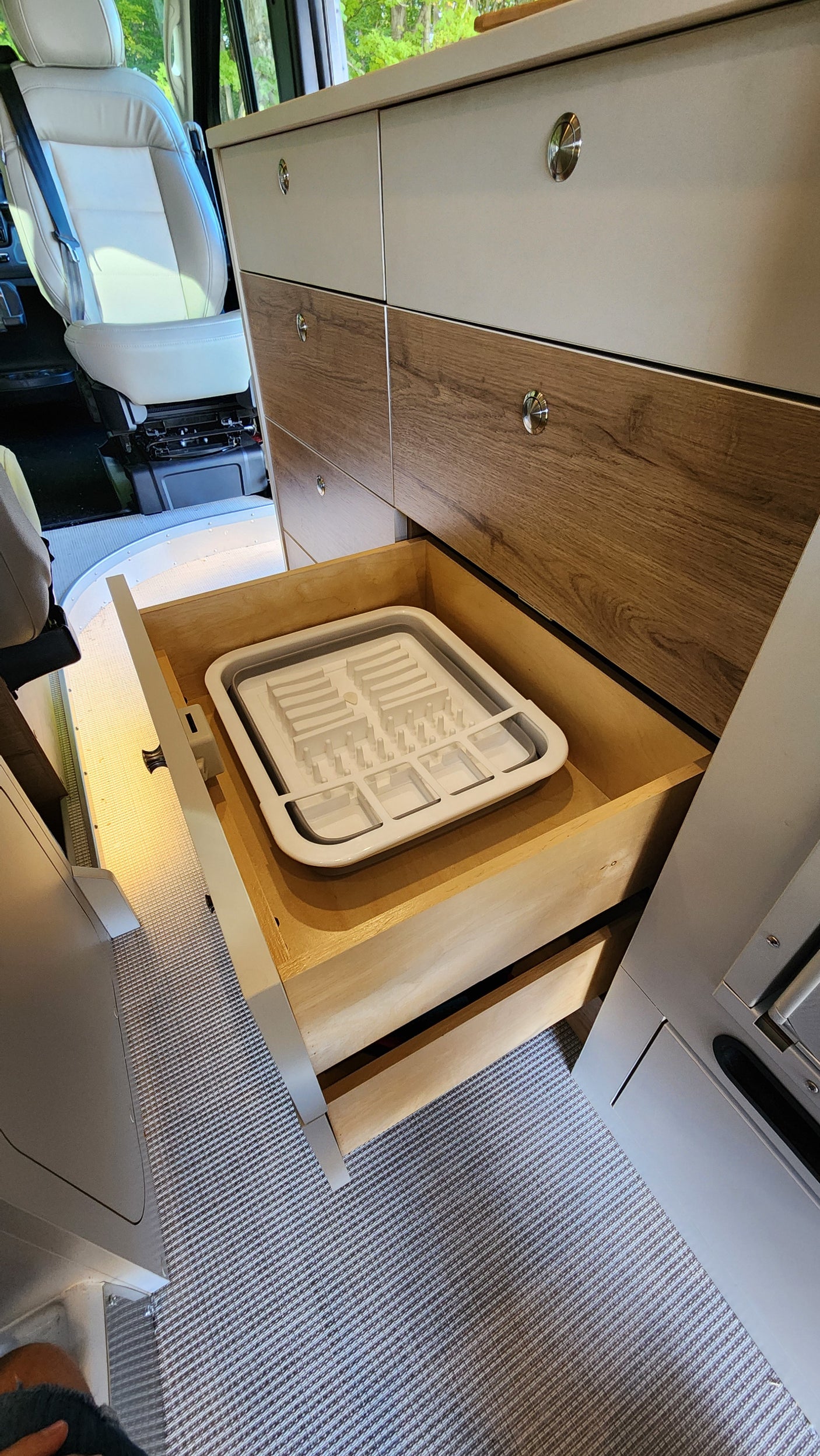 RV rental interior: A multi-drawer cabinet is shown, with one open revealing a white collapsible dish drying rack.