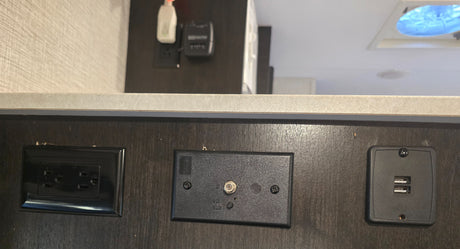 RV rental interior: dark wall panel featuring AC power outlet, coaxial TV connection with antenna booster, and dual USB charging ports.