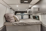 This RV rental's cozy campervan interior features a comfy bed, overhead storage, and ambient lighting.