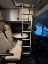 RV rental interior: comfy seating with table, and ladder to upper bunk for adventurers. Ideal camper van space.