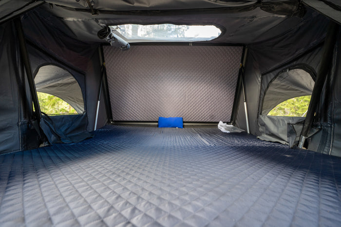 Spacious RV rental interior with a comfortable, gradient quilted mattress, small blue pillow, and side windows showing trees.