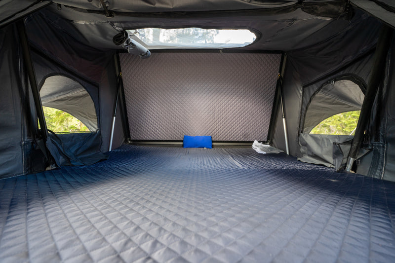 Spacious RV rental interior with a comfortable, gradient quilted mattress, small blue pillow, and side windows showing trees. — photo 5